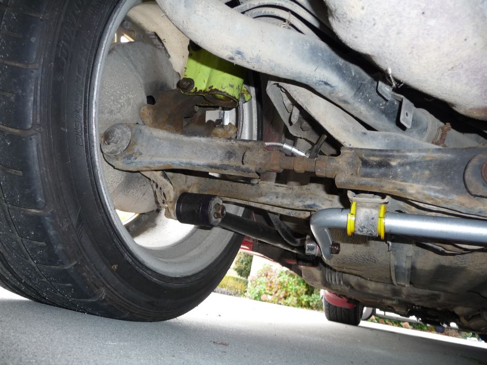 Close-up of a car's rear suspension components including a sway bar with yellow bushings