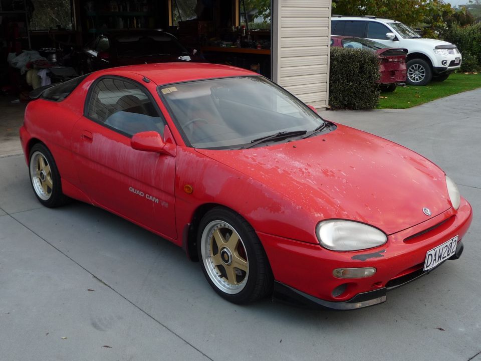 Red 1993 Mazda MX-3 coupe with gold-accented wheels parked on a concrete driveway
