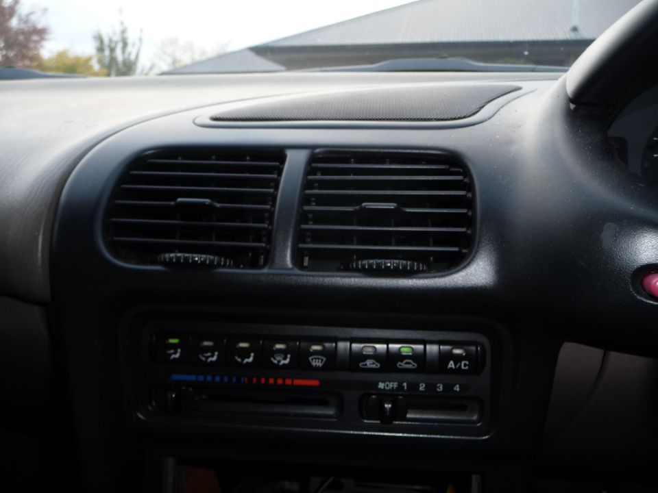 Car dashboard with air vents and climate controls. Shows A/C button and fan speed settings