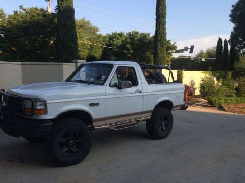 1996 Ford Bronco - White 1996 Ford Bronco with aftermarket wheels and a roll cage is parked outside.