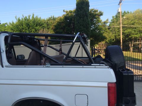 1996 Ford Bronco - The rear section of a white Ford Bronco is shown with a prominent black roll cage and a spare tire cover.