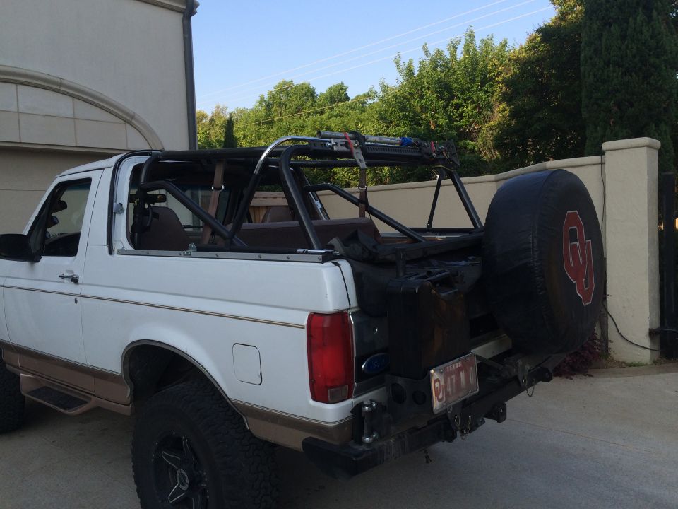 White Ford Bronco with brown trim, aftermarket roll cage, and spare tire cover with OU logo, viewed from the rear