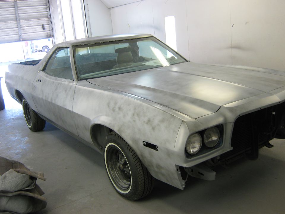 Primer-covered coupe utility vehicle, likely a 1972 Ford Ranchero, in a garage. Front end is partially disassembled