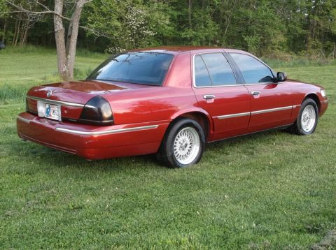 1999 Mercury Grand Marquis - A red sedan with chrome trim and aftermarket wheels is parked on a grassy lawn.