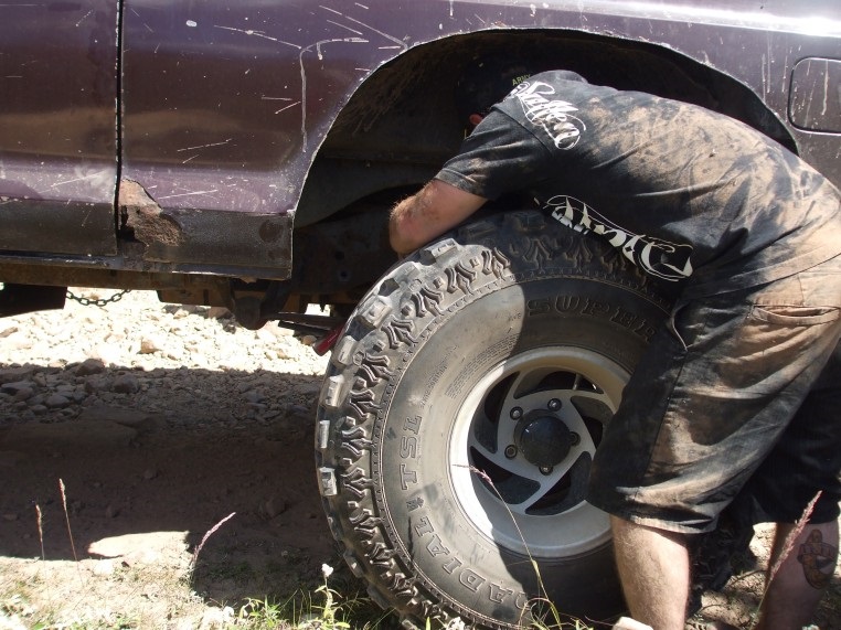 Person reaching into wheel well of a muddy, dark purple SUV with rust on the rocker panel
