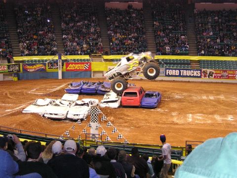1996 Ford Bronco - A monster truck soars through the air above a pile of crushed cars during a show.