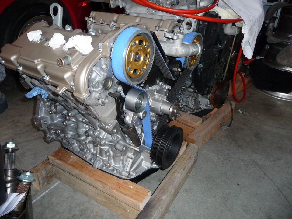 Engine assembly with gold and blue pulleys and blue timing belt, resting on wooden supports