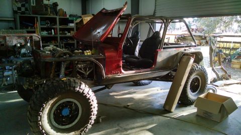 1985 Jeep CJ7 with hood open, doors removed, and roll cage installed, in a garage setting