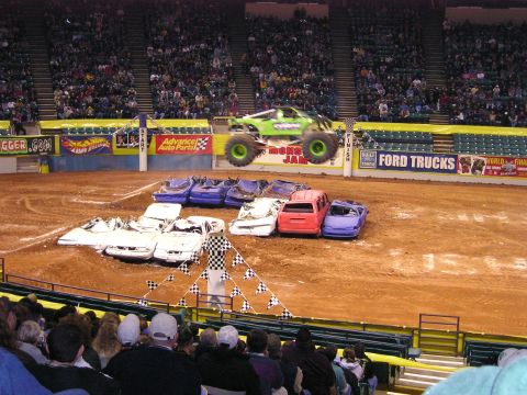 1996 Ford Bronco - A monster truck performs a jump over a row of wrecked cars during a show.