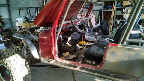 Jeep CJ with hood open, roll cage, and custom fenders. Interior is partially disassembled