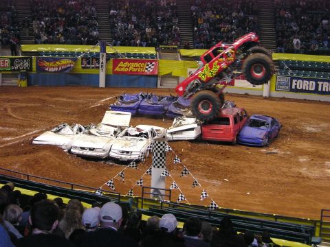 1996 Ford Bronco - A monster truck event with several wrecked cars on the dirt track, and spectators in the stands.