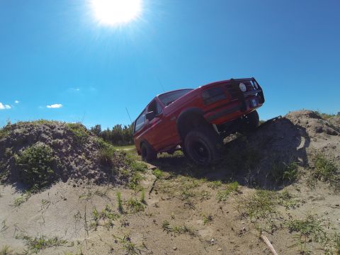 1995 Ford Bronco - A red SUV navigates a sandy incline on a bright, clear day.