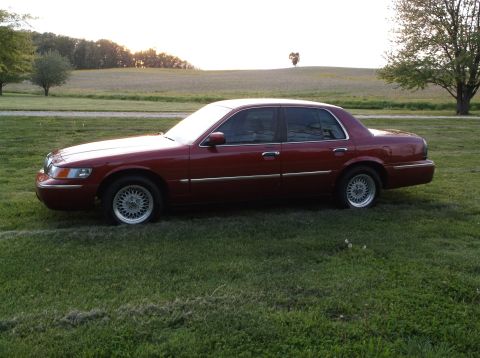 1999 Mercury Grand Marquis - A red 1999 Mercury Grand Marquis sedan is parked on a grassy field during sunset.