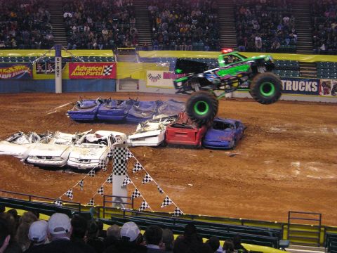 1996 Ford Bronco - A monster truck soars over a pile of wrecked cars during a show.