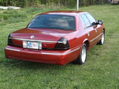 1999 Mercury Grand Marquis - This red sedan is parked on a grassy area with trees in the background.