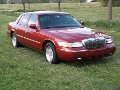 1999 Mercury Grand Marquis - Red sedan with chrome grille and wire wheels parked on a grassy lawn.
