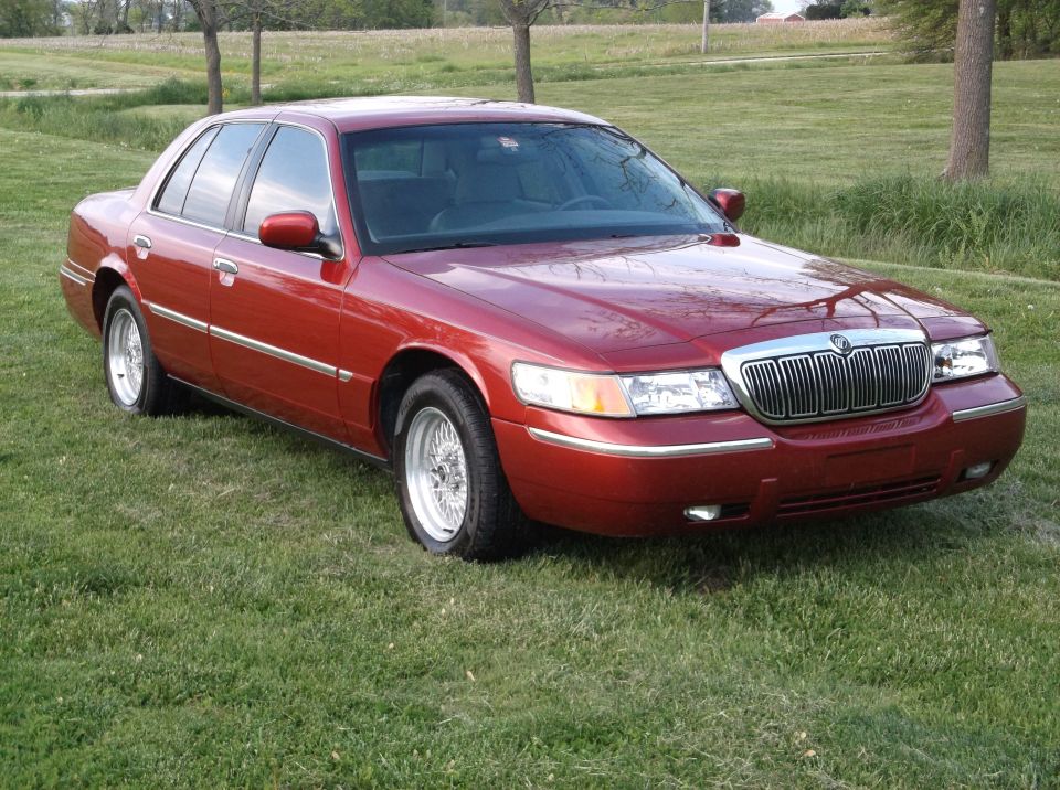Red sedan parked on grass, front 3/4 view. Chrome grille and trim. Wire wheels