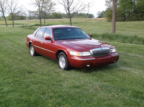 1999 Mercury Grand Marquis - Red sedan parked on grass with trees in the background.