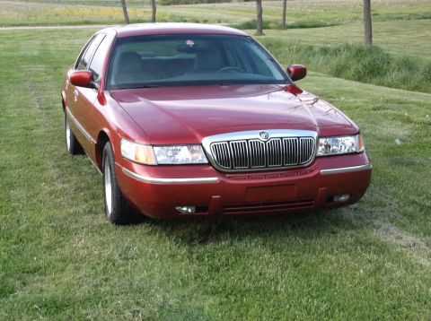 1999 Mercury Grand Marquis - A red sedan with a prominent chrome grille is parked on a grassy area.