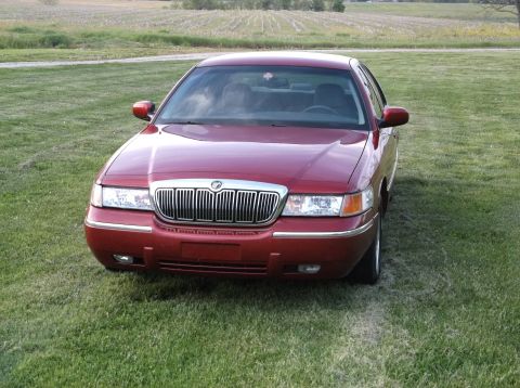 1999 Mercury Grand Marquis - A red 1999 Mercury Grand Marquis sedan is parked on a grassy field, facing the camera.