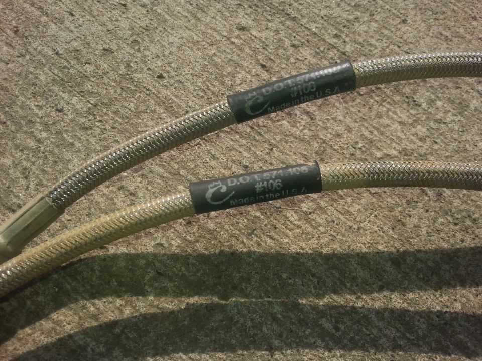 Two braided brake hoses with black bands labeled D.O.T. 1571.106 #106 Made in the U.S.A