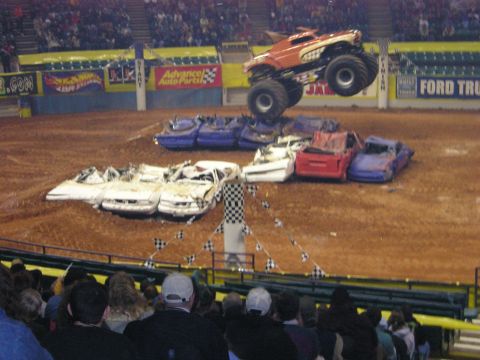 1996 Ford Bronco - A monster truck leaps over a collection of crushed cars during a demolition derby event.