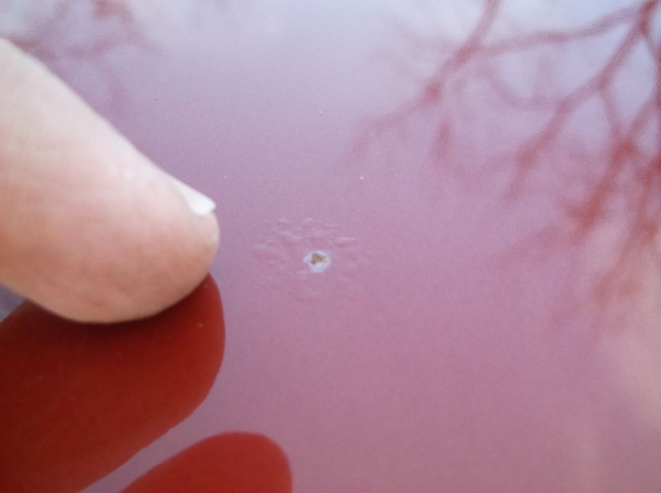 Finger pointing at paint chip on red car