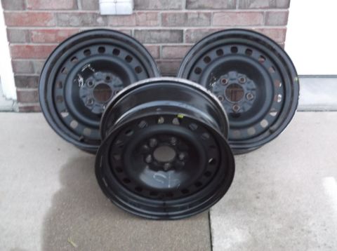 1999 Mercury Grand Marquis - Three black steel wheels are displayed on a concrete surface in front of a brick wall.