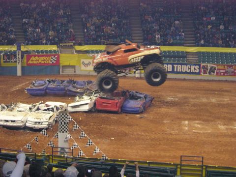1996 Ford Bronco - A monster truck performs a stunt, leaping over a pile of destroyed vehicles in an arena.