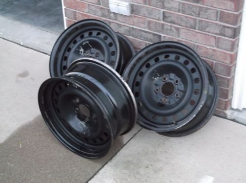 1999 Mercury Grand Marquis - Four black steel wheels are stacked on concrete next to a brick wall.