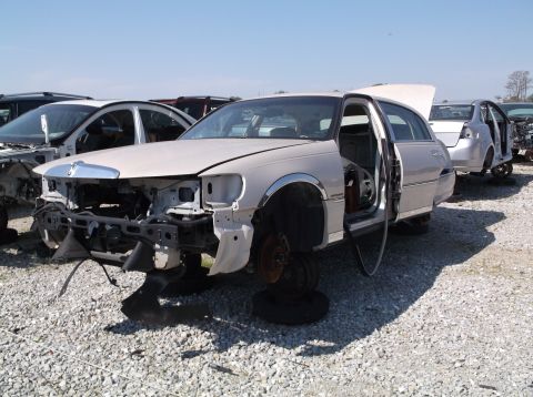 1999 Mercury Grand Marquis - A damaged car sits in a junkyard with its front end dismantled and wheels missing.