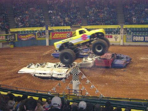 1996 Ford Bronco - A monster truck performs a stunt, leaping over a pile of wrecked cars in an arena.