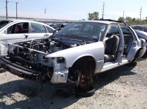 1999 Mercury Grand Marquis - A silver sedan, likely from the early 2000s, sits in a junkyard with its front end dismantled.