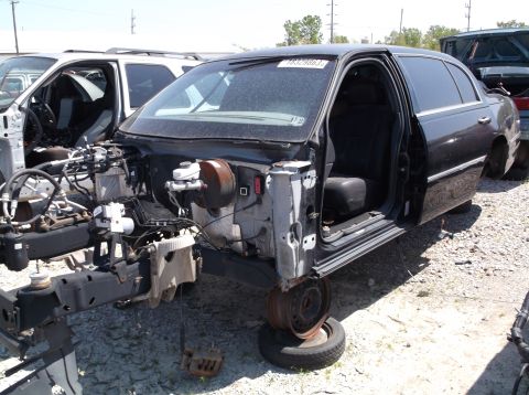1999 Mercury Grand Marquis - Disassembled black sedan in a junkyard, with a white SUV visible in the background.