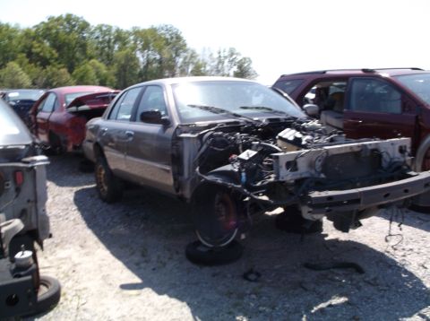 1999 Mercury Grand Marquis - A damaged sedan sits in a junkyard, its engine compartment exposed.
