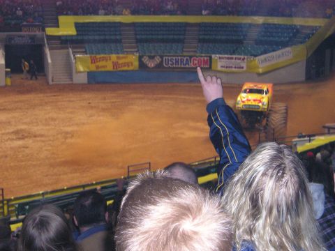 1996 Ford Bronco - A monster truck with flame decals is seen in an arena, with spectators in the foreground.