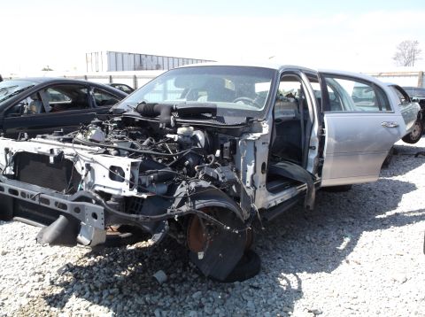 1999 Mercury Grand Marquis - This heavily damaged sedan sits in a junkyard, missing its front bumper and hood.