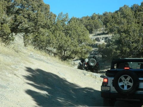 1979 Ford Bronco - Jeeps navigate a rocky, uphill path under a clear blue sky.