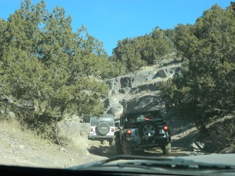 1979 Ford Bronco - Two Jeeps navigate a challenging off-road path through a rocky, wooded landscape.