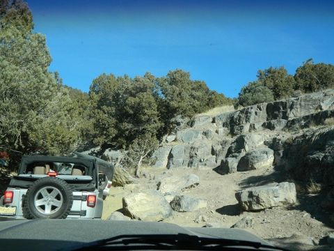1979 Ford Bronco - Jeep Wrangler navigating a challenging rocky trail under a clear blue sky.