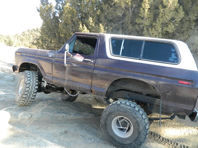 Dark purple and white Ford Bronco with lifted suspension and off-road tires on rocky terrain