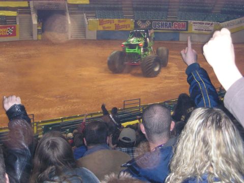 1996 Ford Bronco - A green monster truck performs in an arena, with spectators in the foreground.