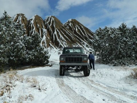 1979 Ford Bronco - A 1979 Ford Bronco navigates a snowy trail with imposing mountains in the background.