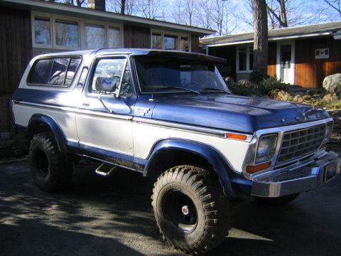 1978 Ford Bronco - A blue and white two-tone full-size Ford Bronco parked in a driveway, shown from the front three-quarter passenger side with FORD lettering…