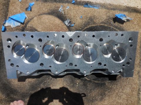 1979 Ford Bronco - Engine cylinder head with visible valves and bolt holes, resting on a textured surface with blue tape fragments.