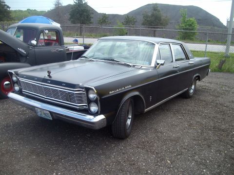 2004 Ford Crown Victoria - A classic Ford Galaxie 500 sedan is parked next to a pickup truck, with a pile of coal in the background.