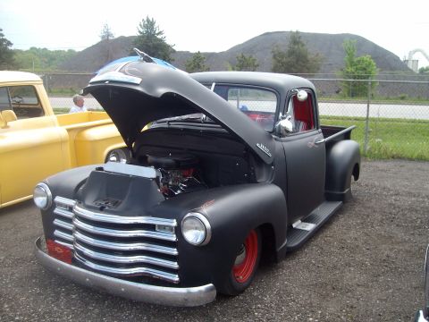 2004 Ford Crown Victoria - A matte black pickup truck with its hood open and red wheels is parked next to a yellow truck.