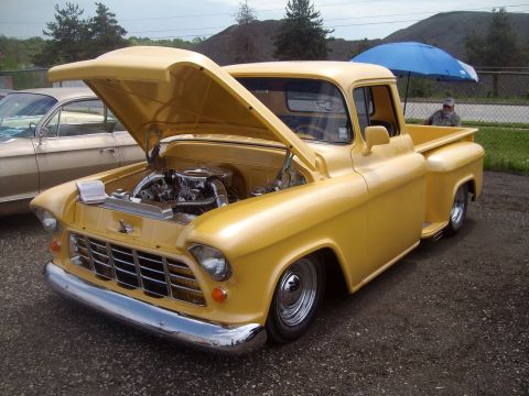 2004 Ford Crown Victoria - A yellow 1950s pickup truck is displayed with its hood open, revealing the engine. Another vehicle is parked nearby.