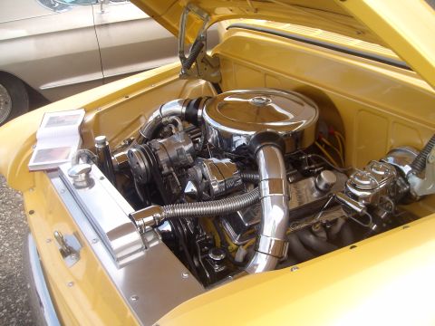 2004 Ford Crown Victoria - The engine bay of a yellow vehicle is open, revealing a chrome-detailed engine and a book on the radiator.