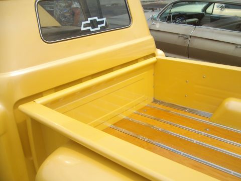2004 Ford Crown Victoria - A yellow pickup truck bed with a wood floor and chrome strips is visible, alongside a Chevrolet emblem on the rear window and a vintage car…